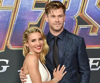 Couple smiling on a red carpet event with a movie poster in the background.