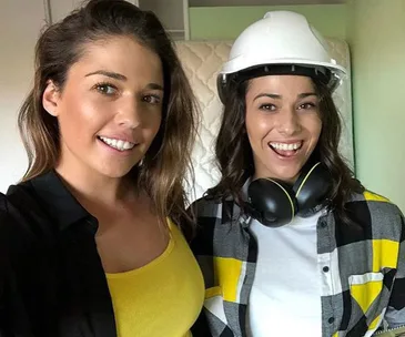 Two women smiling; one wearing a hard hat and headphones, the other in a yellow top.