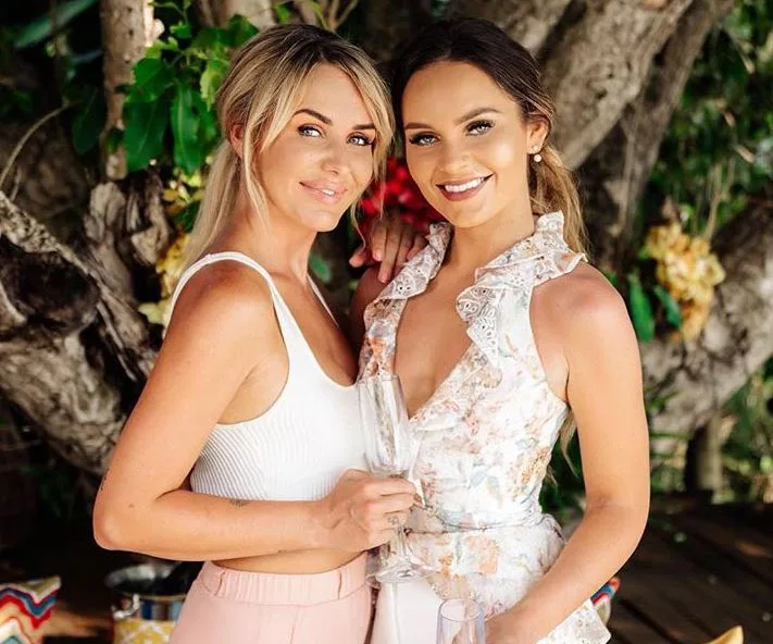 Two women smiling and posing with champagne glasses at an outdoor event.