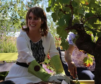 Woman in a white dress and green gloves gardening, smiling in bright sunlight.
