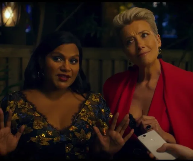 Two women talking, one with dark hair in a floral dress and the other with short hair in a red outfit, holding a phone.
