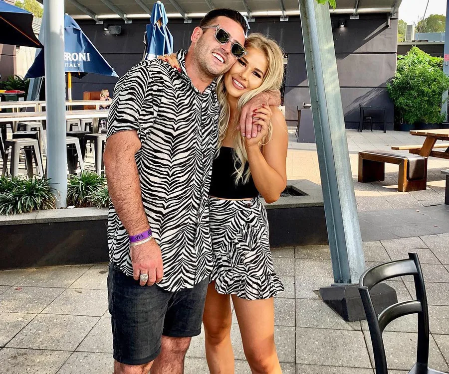 Zebras print clothing couple smiling, arms wrapped, at outdoor venue.