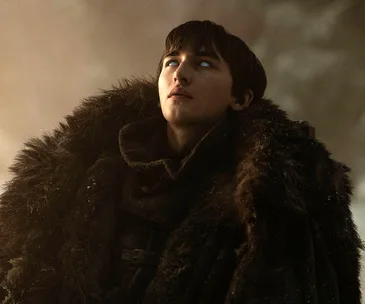 Bran Stark from Game of Thrones looks upwards, wearing a fur cloak with glowing eyes, shrouded in misty surroundings.