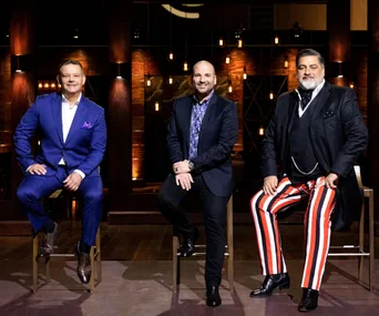 Three judges from MasterChef Australia 2019 sit on stools, wearing distinctive suits, against a dimly lit backdrop.