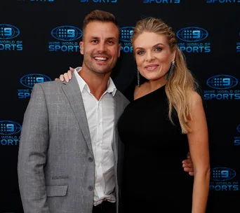 Man in a gray suit and woman in a black dress posing together at Wide World of Sports event backdrop.