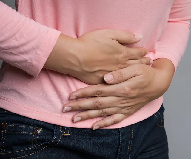 Person in a pink shirt clutching their stomach, possibly indicating discomfort or pain.