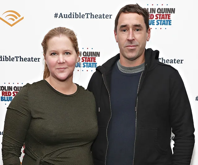 Couple posing at the Audible Theater event for Colin Quinn's Red State Blue State, in front of a branded backdrop.