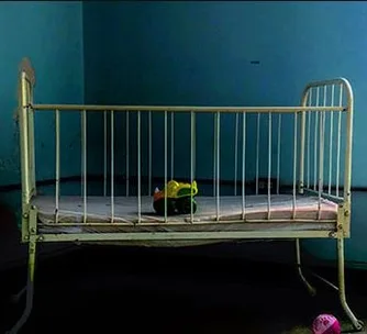 Old metal crib in a dimly lit room with a colorful toy duck on the mattress.