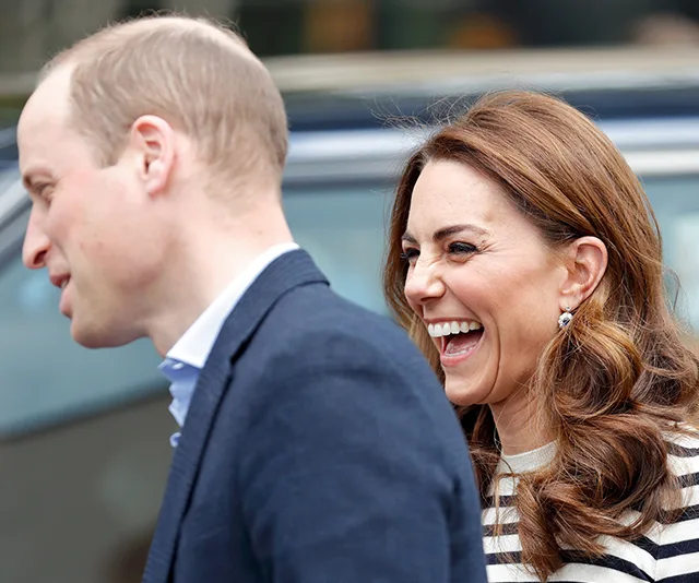 Prince William and Kate Middleton smiling while walking outside together.