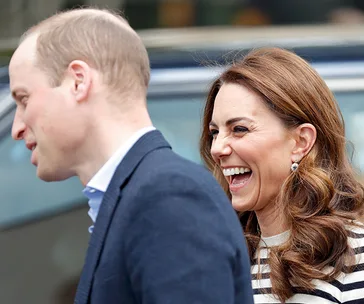 Prince William and Kate Middleton smiling while walking outside together.