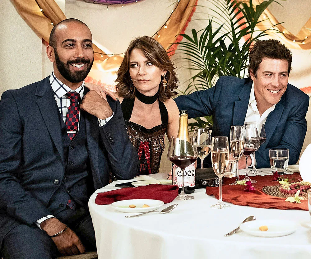 Three people sit smiling at a decorated table with drinks and a festive background.