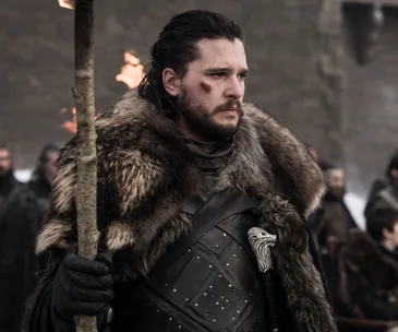 A man in fur armor holds a torch, with a determined expression and a scarred cheek, standing in a medieval setting.