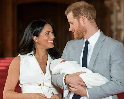 A couple smiling at each other while holding a newborn wrapped in a white blanket.
