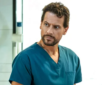 Doctor in blue scrubs from "Harrow," looking serious.