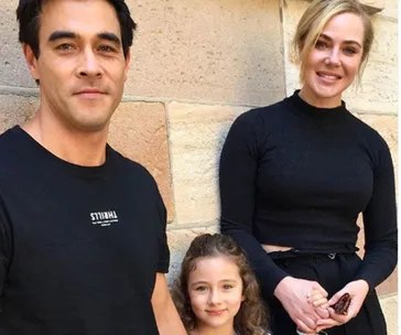 Family portrait with a man, woman, and child smiling against a stone wall.