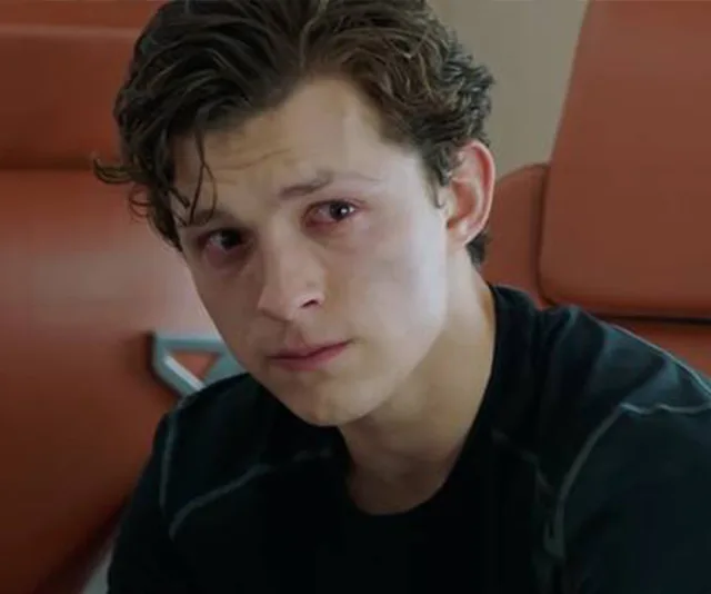 Young man, with red eyes, in a thoughtful pose, sits on an orange seat, wearing a black shirt.