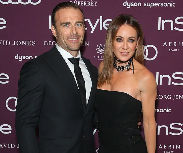 Two people posing together at an event, in formal attire with purple InStyle backdrop.