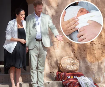 Couple in light attire stand outside, gesturing; inset shows baby swaddled in white with hands gently holding.