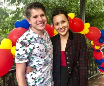 A smiling couple stands in front of colorful balloons in a garden setting.