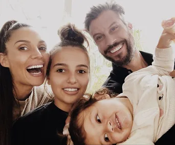 A happy family of four posing together; the parents smiling alongside their two children, with one child being held playfully.