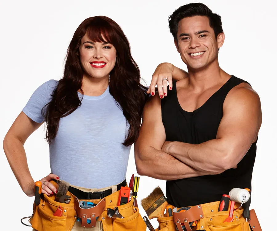 A woman in a light blue shirt and a man in a black tank top, both wearing tool belts, smiling confidently.