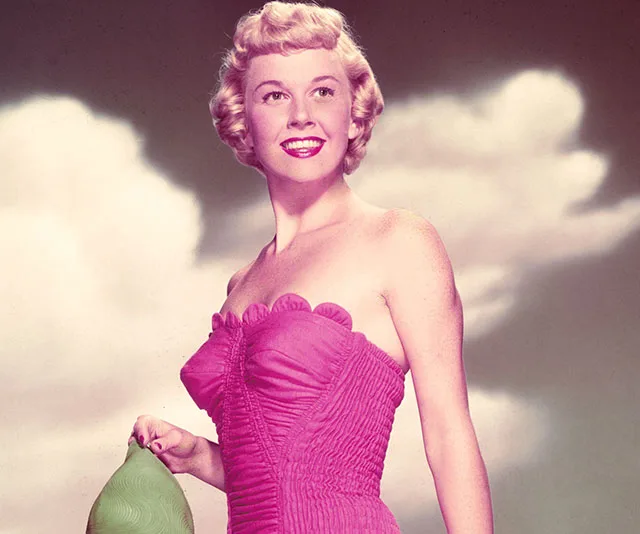 Woman in a pink dress holding a green object, smiling against a cloudy sky background.