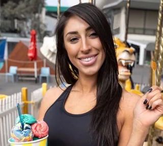 A smiling woman with long dark hair holds a colorful ice cream cone at an outdoor amusement park.