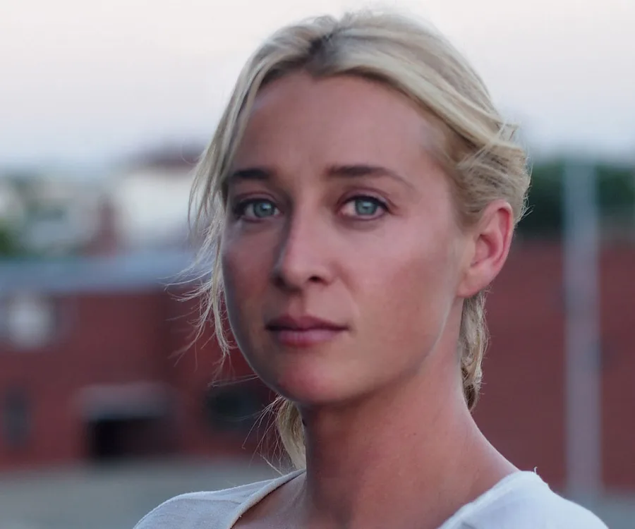 Portrait of a woman with blonde hair and blue eyes, looking serious outdoors.