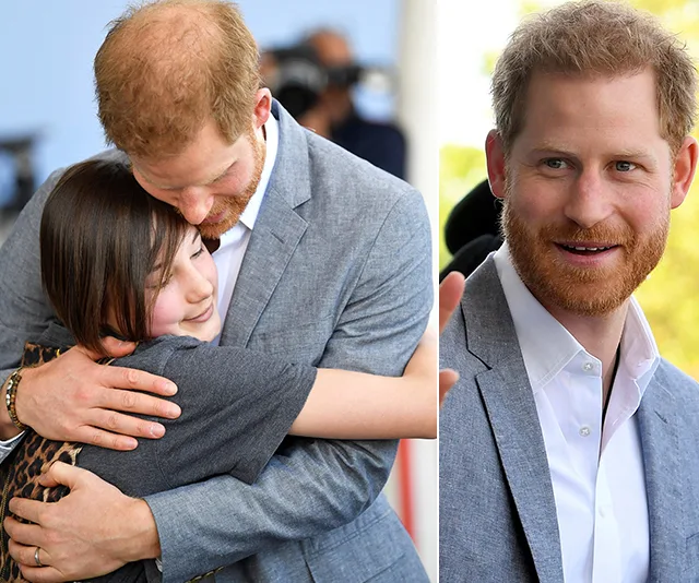 Prince with red hair embraces a person affectionately; close-up of him smiling in a gray suit and white shirt.