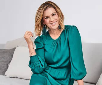 A woman in a green dress sits and smiles on a couch with grey and white cushions.