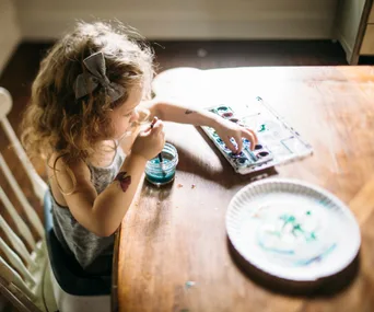 A toddler painting with watercolors at a wooden table, focusing on creative play.