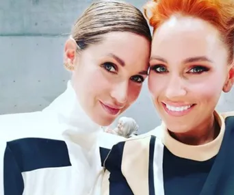 Two women smiling at the camera, dressed in black and white outfits, against a plain background.