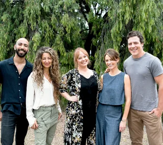 Group of five people smiling, standing outdoors with trees in background.
