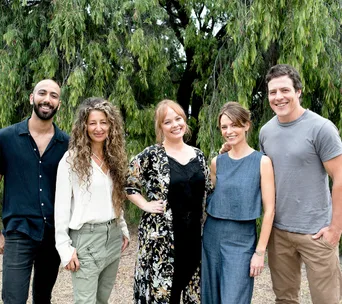 Group of five people smiling, standing outdoors with trees in background.