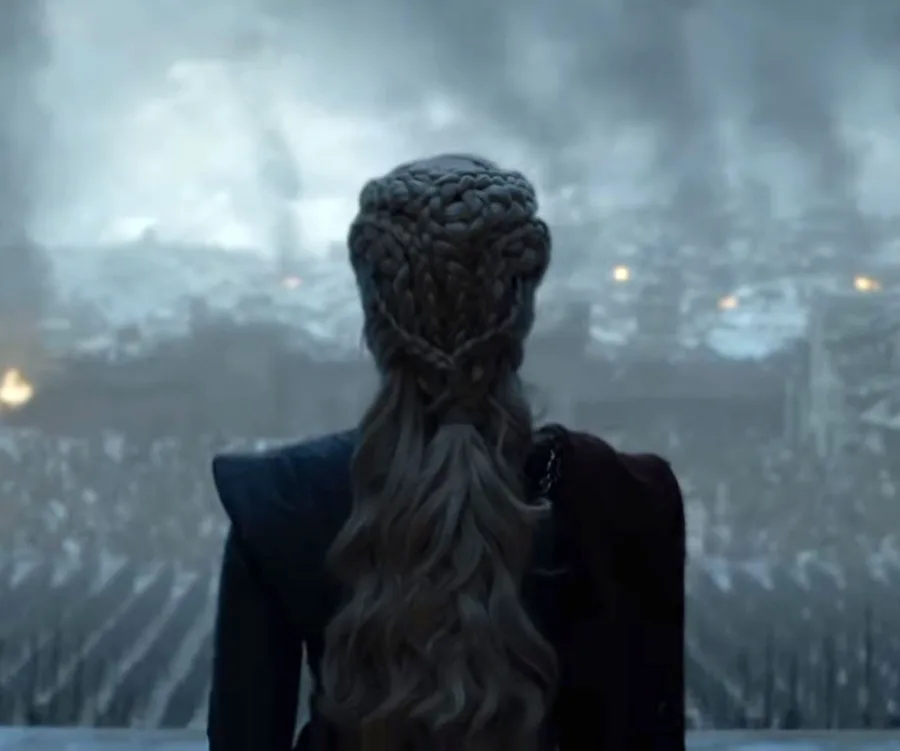 Daenerys Targaryen stands facing a smoke-filled, ruined city with braided hair in "Game of Thrones" finale scene.