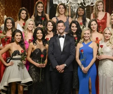 A group photo from The Bachelor with contestants holding roses, standing around the host in formal wear.