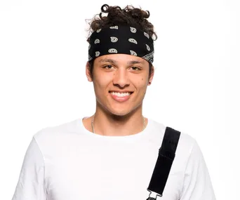 Rapper in a white shirt with a black bandana smiles confidently at the camera.