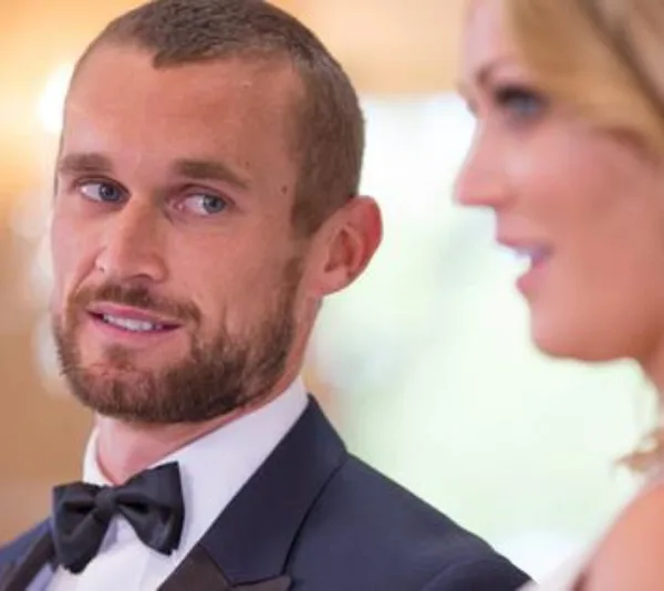 Man in a suit looks intently at a woman, who is partially visible, against a blurred background.