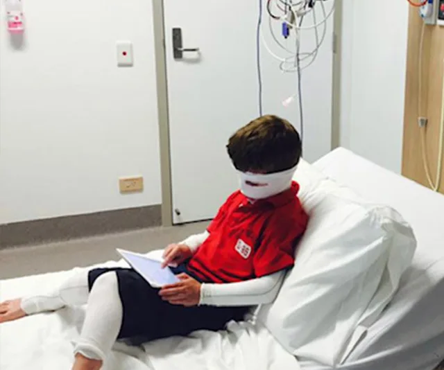 Boy with bandages sitting on a hospital bed using a tablet.
