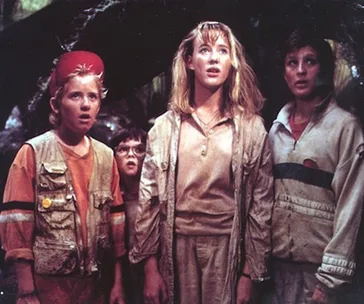 Children from "Honey, I Shrunk the Kids" look amazed in an outdoor setting, wearing casual, slightly soiled clothes.