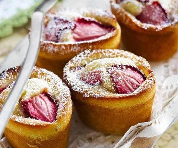 Four golden brown strawberry friands topped with powdered sugar on a decorative tray.