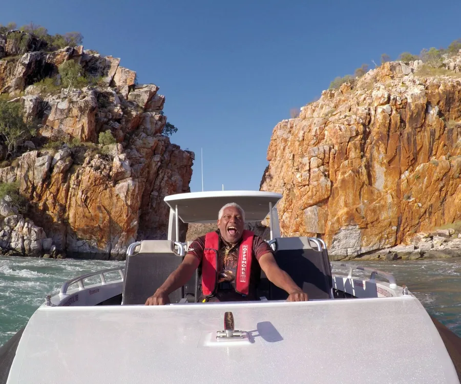 Man joyously steering a boat through a rugged rock formation under a clear blue sky.