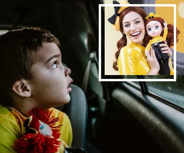 Boy in a car holds a "Wiggles" doll, looking at a photo of a smiling woman in yellow, also holding a similar doll.