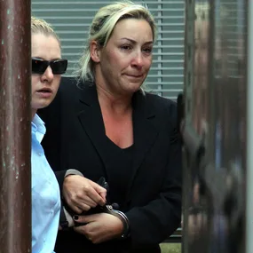 Two women, one in handcuffs, walk closely together outdoors, with one wearing sunglasses.