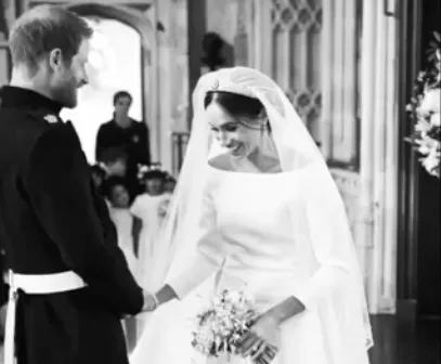 Meghan Markle and Prince Harry smiling and holding hands at their wedding ceremony, surrounded by bridesmaids.