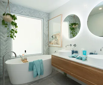 Modern bathroom with a freestanding bathtub, plants, and double vanity with round mirrors.
