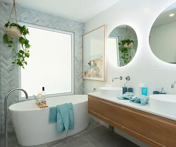 Modern bathroom with a freestanding bathtub, plants, and double vanity with round mirrors.