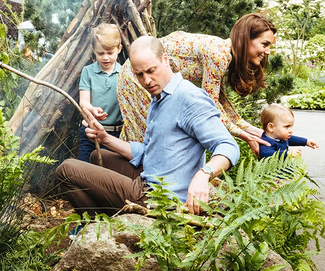 A family with two children exploring a garden, surrounded by greenery and a wooden structure.