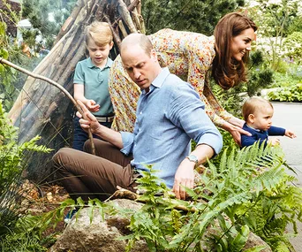 A family with two children exploring a garden, surrounded by greenery and a wooden structure.
