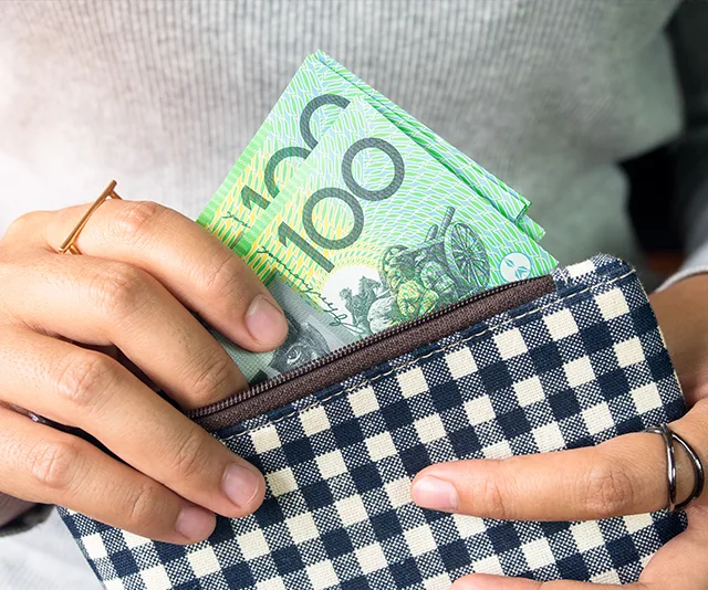A person placing Australian 100-dollar bills into a checkered wallet.